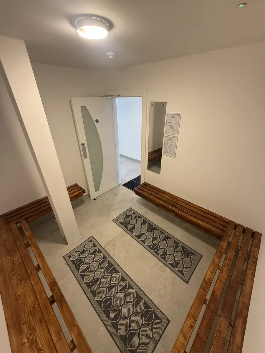 Changing room: pine benches along both walls and patterned mats on a pale stone floor, the door out to the corridor