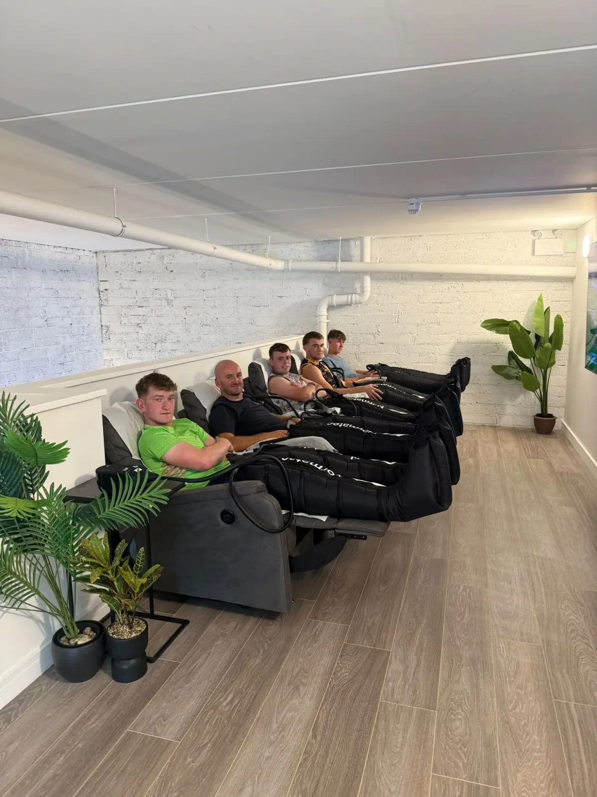 Five guests in the recliners with the boots on, the white brick wall and a palm behind them