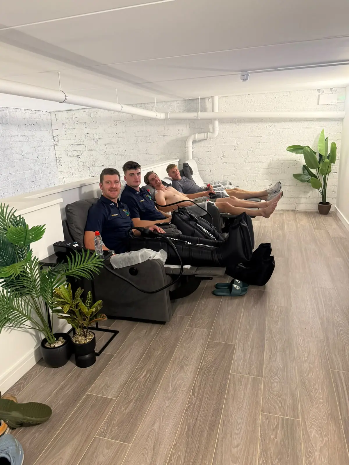 Three guests reclining in the compression lounge, the TV on the far wall