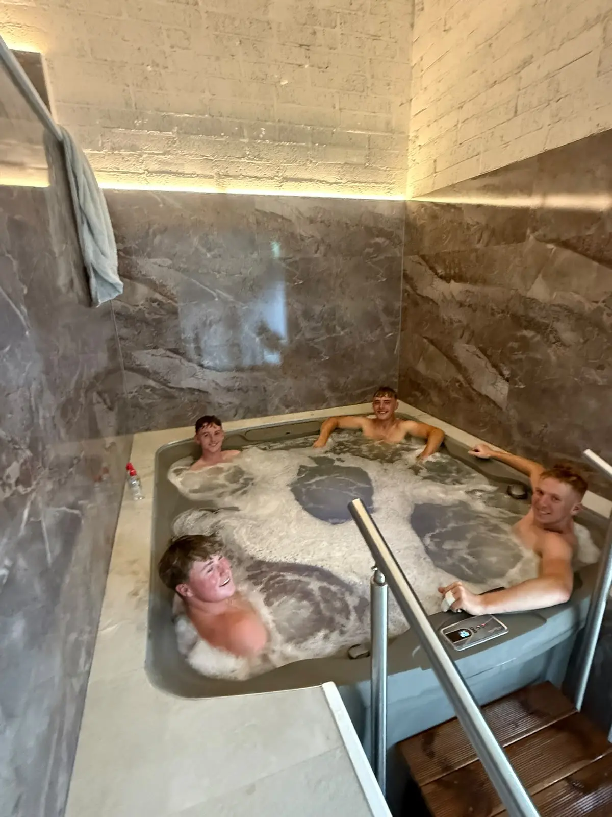 Three guests in the jacuzzi, the marble walls and the steel handrail beside them