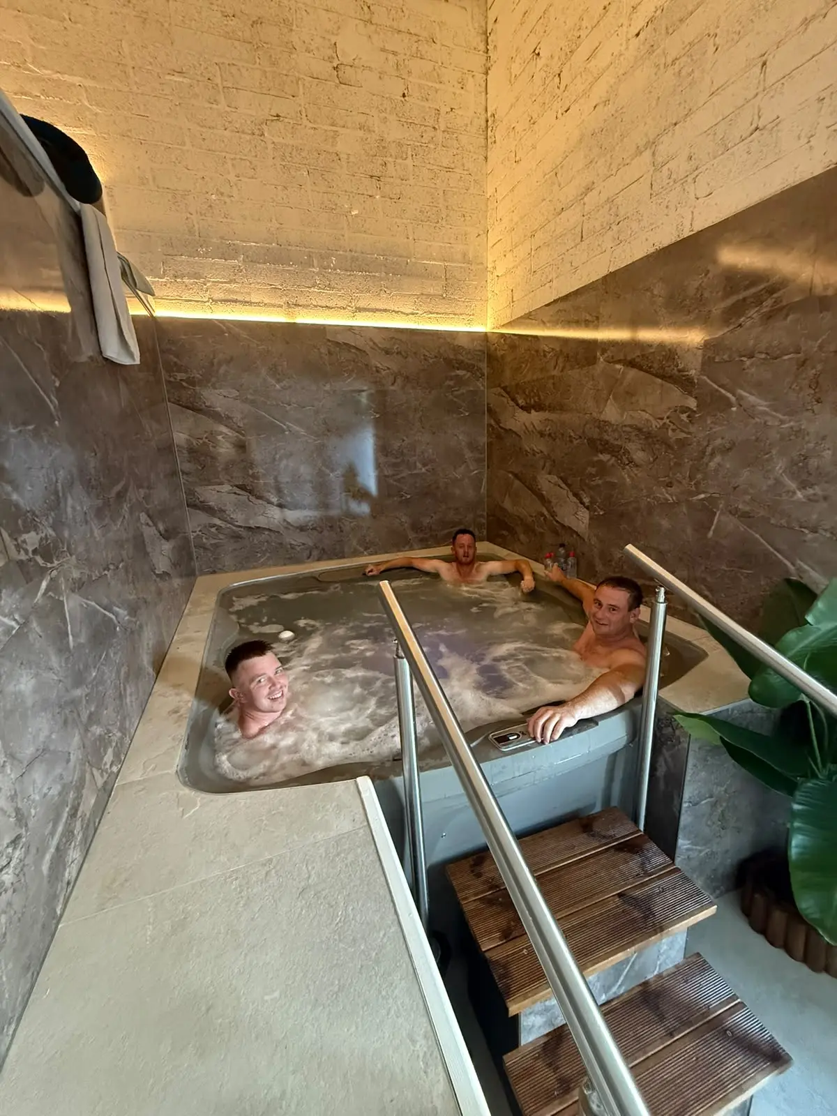 Two guests in the jacuzzi seen from the steps, warm light along the top of the marble wall