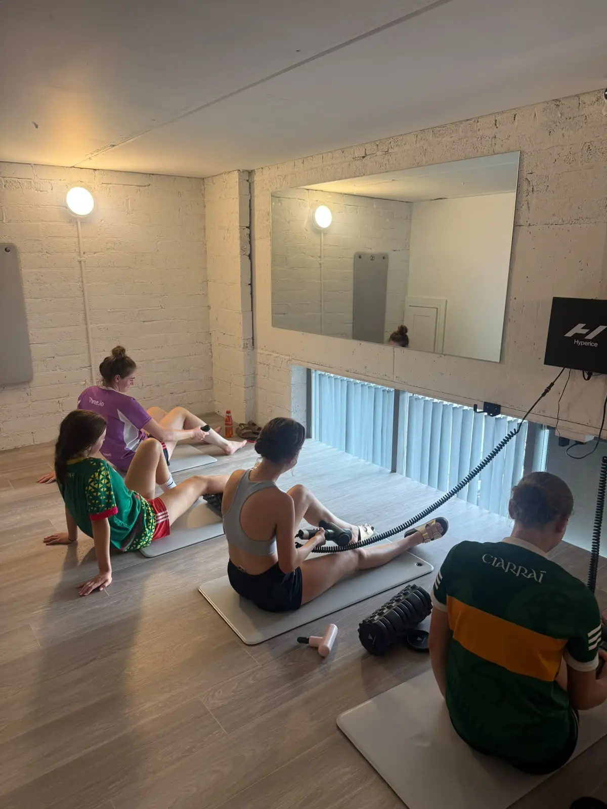 Guests on mats using the massage guns, the mirror wall behind them