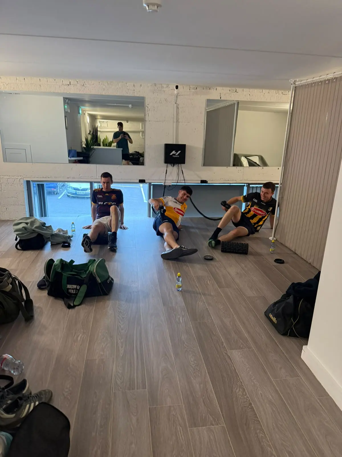 Two guests sitting on the floor with foam rollers and a massage gun, kit bags by the door