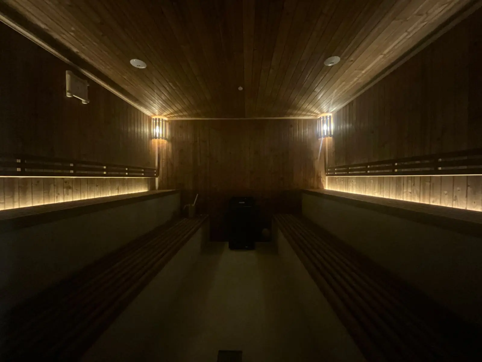 The sauna at night: two wall lamps glowing on the pine walls, the benches lit from below, the heater at the end