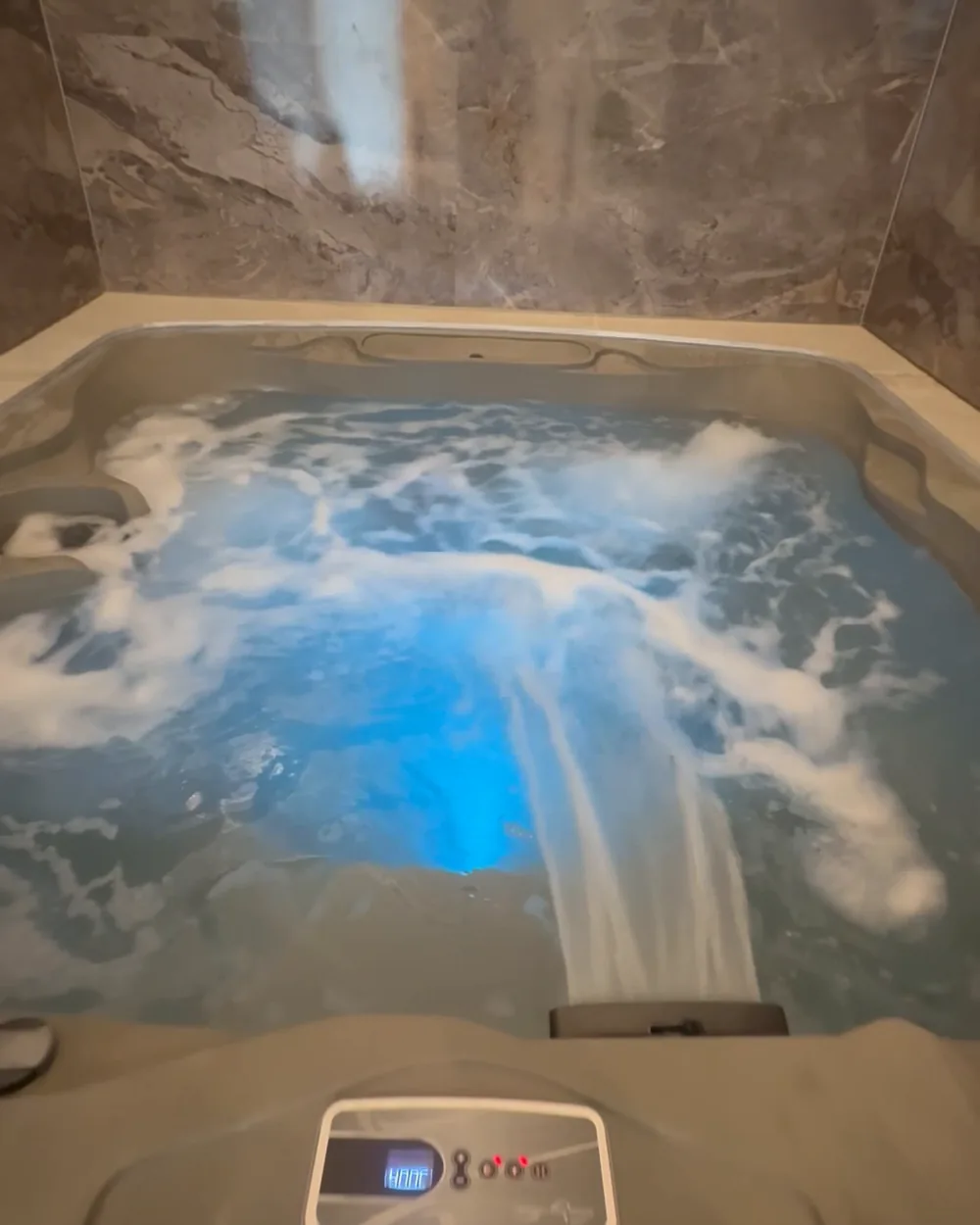 The jacuzzi: jets churning the blue-lit water beneath grey marble walls, the control panel at the near edge